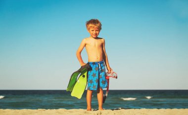 Dalgıç maskeli ve yüzgeçli küçük çocuk plajda yüzmeye gider.