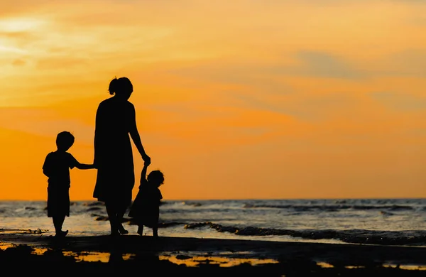 Mãe e dois filhos andando na praia ao pôr do sol — Fotografia de Stock