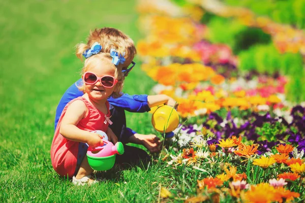 Klein meisje en jongen drenken bloemen in tuin — Stockfoto
