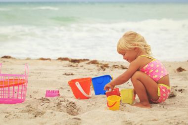 Tatlı küçük kız kumsalda kumla oynuyor.
