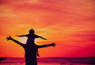 Baba ve küçük oğlu günbatımı plaj üzerinde oynamak