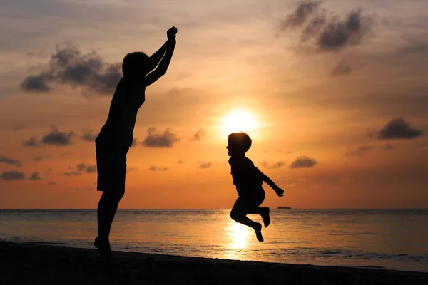 Feliz pai e filho pulando na praia do pôr do sol — Fotografia de Stock