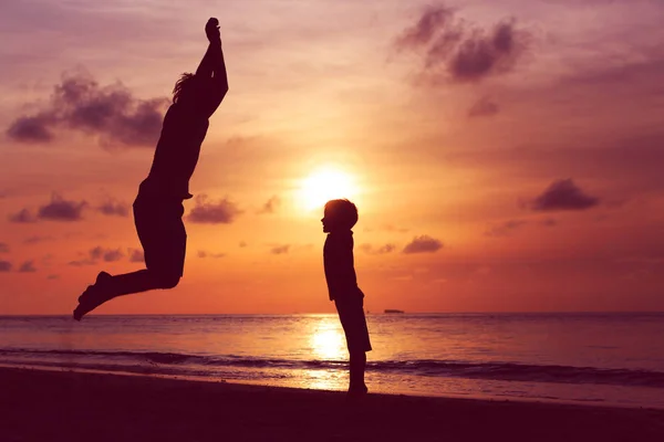 Szczęśliwy ojciec i syn skoki w sunset beach — Zdjęcie stockowe