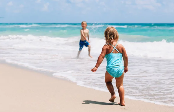 Małej dziewczynki i chłopiec uruchomić grę z fale na plaży — Zdjęcie stockowe