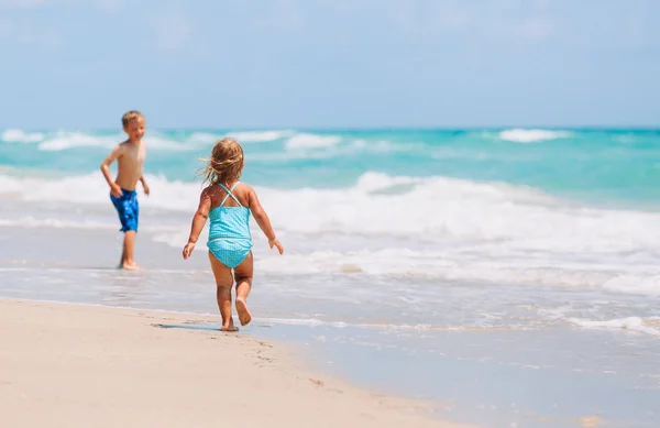 Małej dziewczynki i chłopiec uruchomić grę z fale na plaży — Zdjęcie stockowe