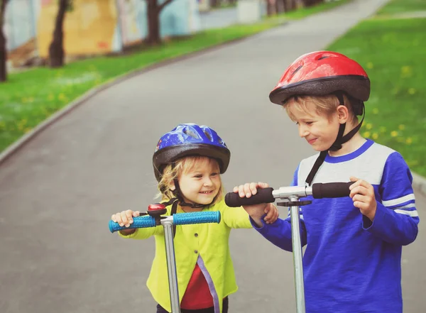 Menino e menina com capacetes equitação scooters — Fotografia de Stock