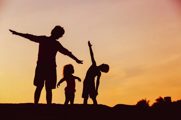 Батько з сином і дочкою силуети грають на заході сонця — стокове фото