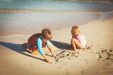Küçük oğlan ve kız kumsalda kumla oynuyorlar.