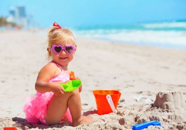 Tatlı küçük kız kumsalda kumla oynuyor.