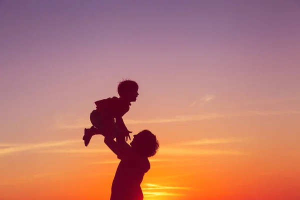 Vader en kleine zoon silhouetten spelen bij zonsondergang — Stockfoto