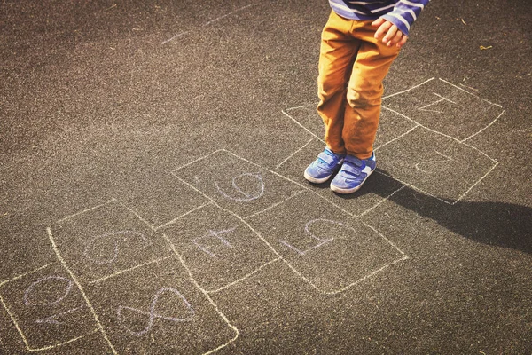 Pequeno menino jogar hopscotch no playground — Fotografia de Stock