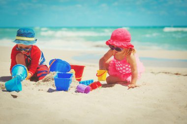 Küçük oğlan ve kız kumsalda kumla oynuyorlar.