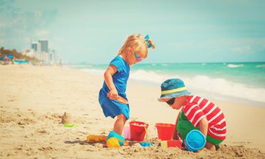 Küçük oğlan ve kız kumsalda kumla oynuyorlar.