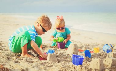 Küçük oğlan ve kız kumsalda kumla oynuyorlar.