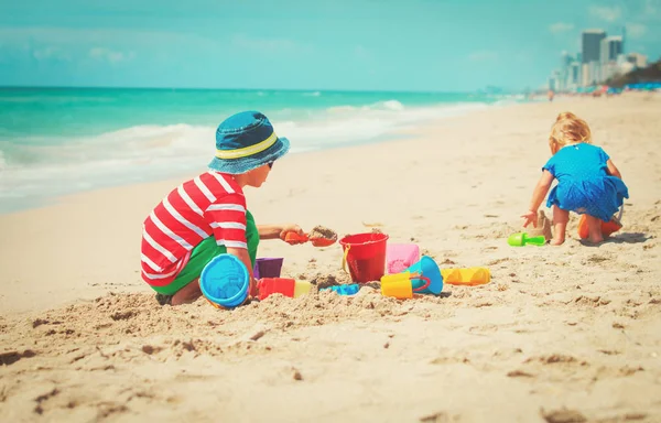 Niño y niña juegan con arena en la playa — Foto de Stock