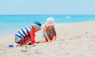 Küçük oğlan ve kız kumsalda kumla oynuyorlar.