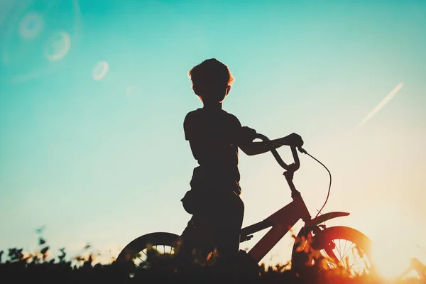 Menino pedalando bicicleta ao pôr do sol — Fotografia de Stock