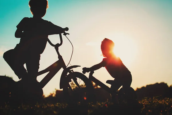 Menino e menina andando de bicicleta ao pôr do sol — Fotografia de Stock