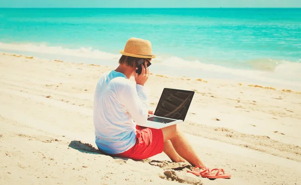 Человек с ноутбуком и мобильным телефоном на пляже — стоковое фото