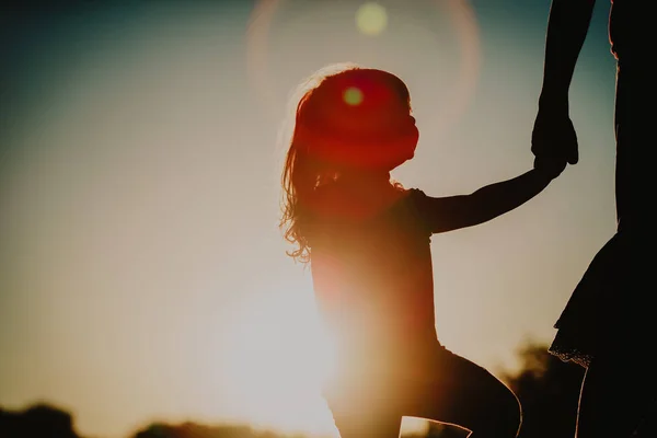 Silhouet van meisje die moeder hand bij zonsondergang — Stockfoto
