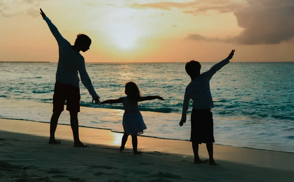 Padre con hijo e hija siluetas jugar al atardecer playa — Foto de Stock