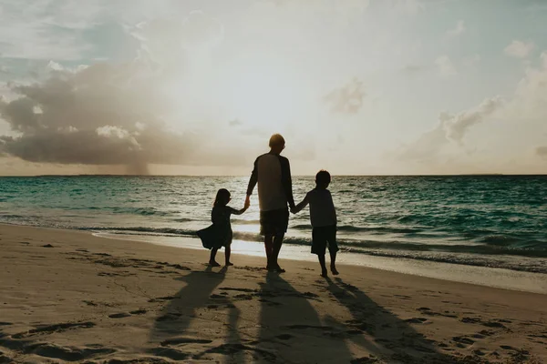 Pai com dois filhos andando na praia ao pôr do sol — Fotografia de Stock