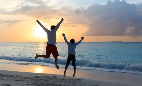 Padre e figlio che saltano alla spiaggia al tramonto — Foto Stock