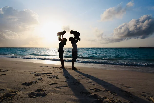 Famille heureuse avec deux enfants sur le jeu sur la plage du coucher du soleil — Photo