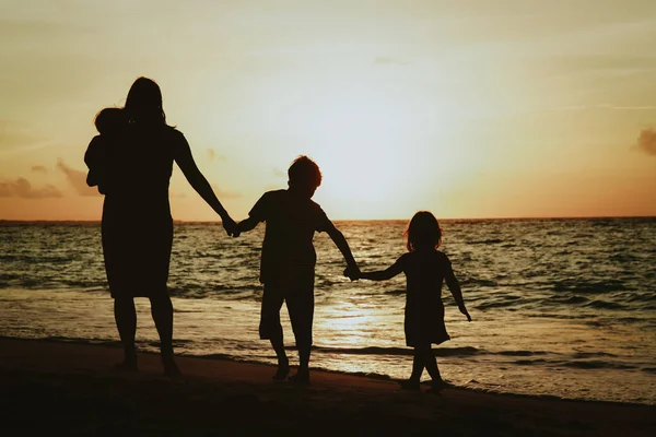 Mère avec trois enfants marchant sur la plage au coucher du soleil — Photo