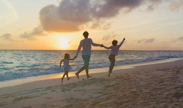 Vader met twee kinderen spelen op het strand bij zonsondergang — Stockfoto