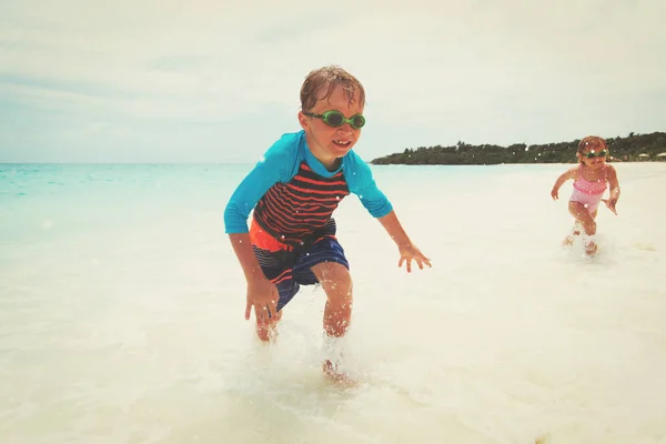 Małej dziewczynki i chłopiec uruchomić grę z fale na plaży — Zdjęcie stockowe