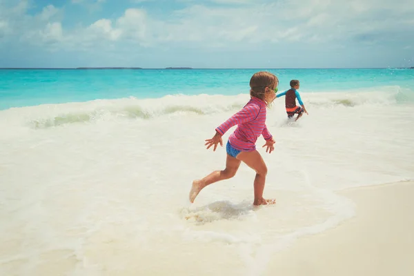 Małej dziewczynki i chłopiec uruchomić grę z fale na plaży — Zdjęcie stockowe