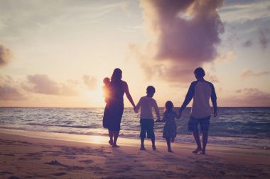 Ağaç çocukları olan mutlu aile gün batımında sahilde yürür.