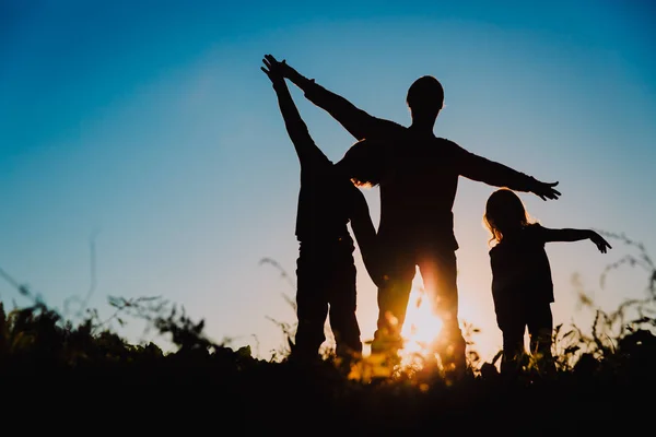 Vader en zoon en dochter silhouetten spelen bij zonsondergang — Stockfoto