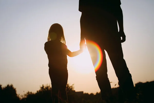 Silhuett av liten flicka som håller föräldrarnas hand vid solnedgången — Stockfoto