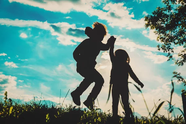 Silueta de niño feliz y niña jugar al atardecer — Foto de Stock