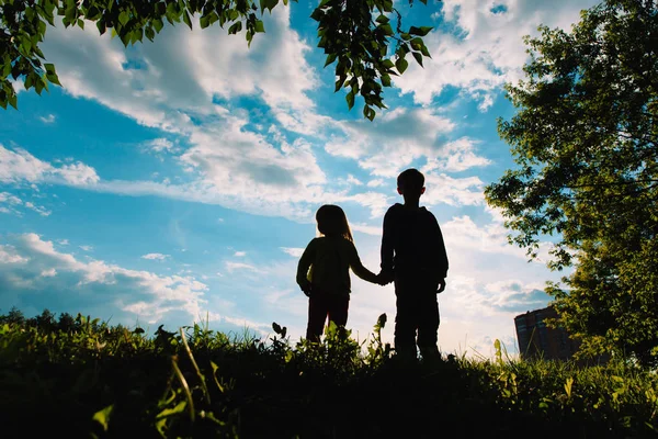 Silhouette di bambino e ragazza che si tiene per mano al tramonto — Foto Stock