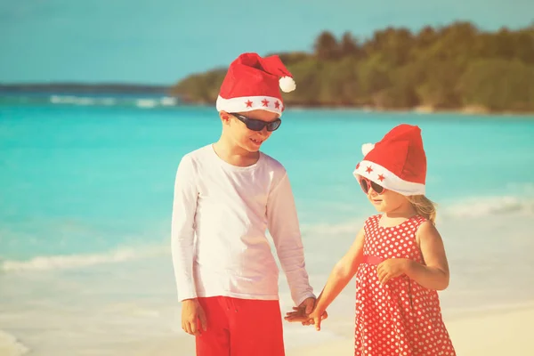 Mały chłopiec i dziewczynka w santa kapelusze zabawy na tropikalnej plaży na Boże Narodzenie — Zdjęcie stockowe