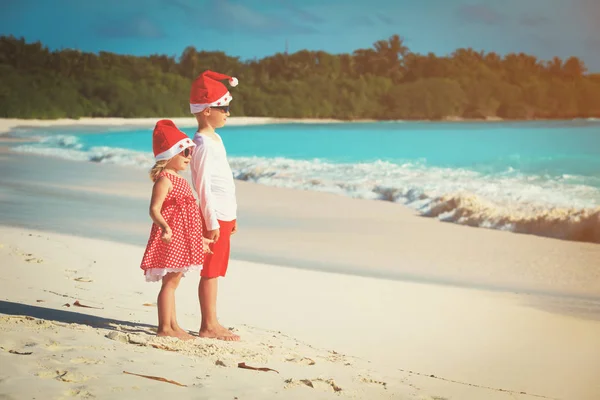 Menino e menina em santa chapéus se divertindo na praia tropical no Natal — Fotografia de Stock