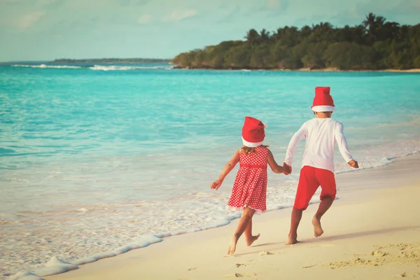 Mały chłopiec i dziewczynka w santa kapelusze zabawy na tropikalnej plaży na Boże Narodzenie — Zdjęcie stockowe