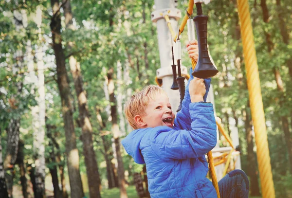 Счастливый маленький мальчик забирается на открытую игровую площадку — стоковое фото