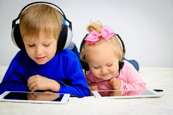 Niño y niña con auriculares mirando la almohadilla táctil —  Fotos de Stock