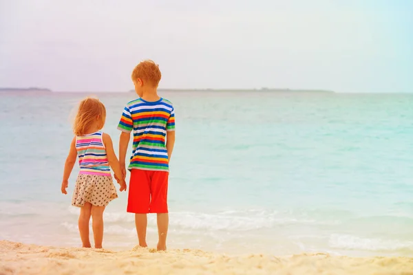 小男孩和蹒跚学步的女孩，手牵着手走在沙滩上 — 图库照片
