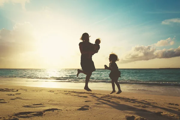 Mutter mit Kindern spielt am Strand bei Sonnenuntergang — Stockfoto