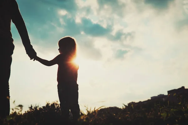 Silueta de niña sosteniendo la mano del padre al atardecer — Foto de Stock