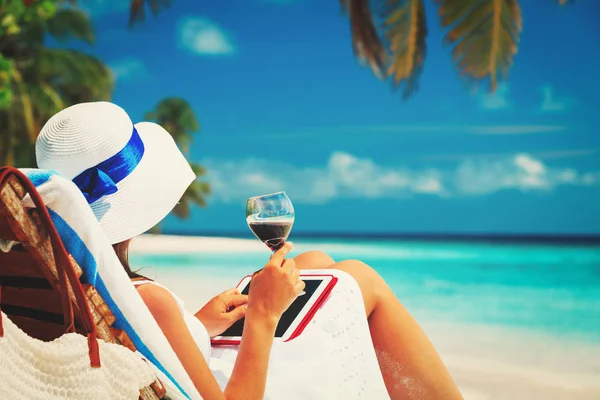 Mujer con almohadilla táctil beber vino en la playa —  Fotos de Stock