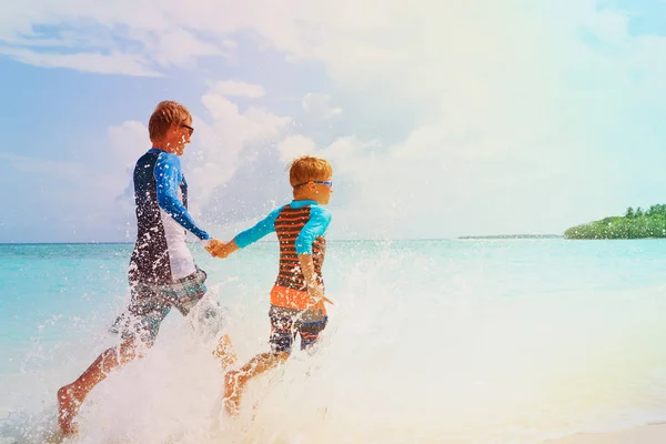 Vader en zoon spelen met water lopen op strand — Stockfoto