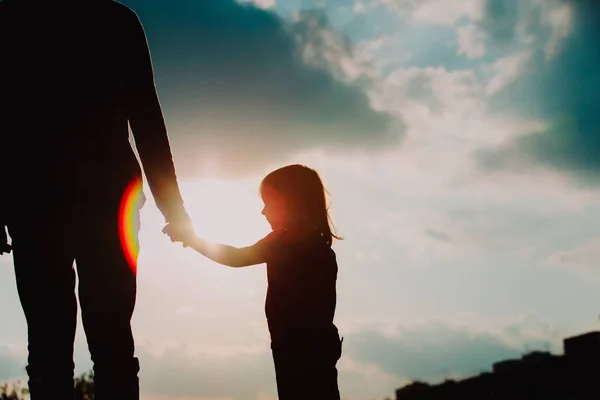 Silhouette of little girl holding parent hand at sunset — стоковое фото