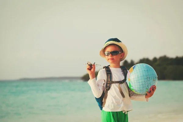 Маленький мальчик с глобусом и игрушечным самолетом путешествует по пляжу — стоковое фото