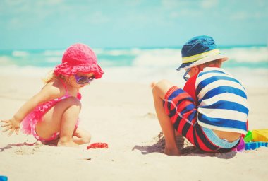 Küçük oğlan ve kız kumsalda kumla oynuyorlar.